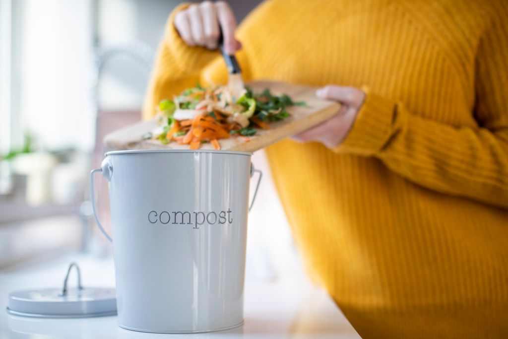 A close up of a woman scraping vegetable sraps into a compost bin