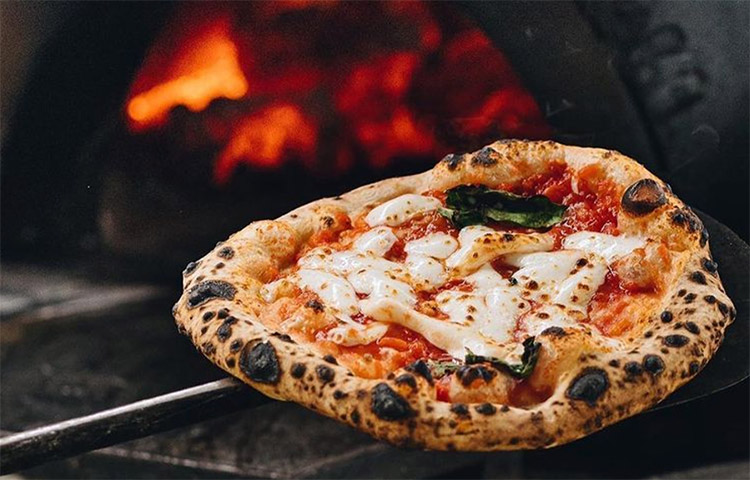pizza-oven margherita pizza being put in the pizza oven