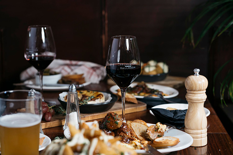 brunswick-ballroom-restaurant two glasses of wine and a beer sitting on a table with 4 different meals at the brunswick ballroom restaurant