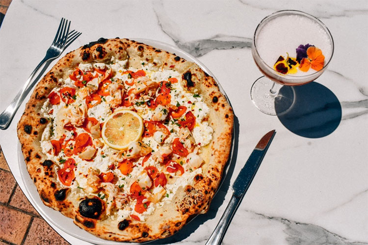pizza-from-400-gradi a whole pizza sitting on a marble table with a cocktail on the side